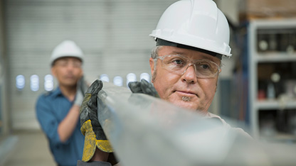 Robotnicy przemysłowi niosący stalową belkę